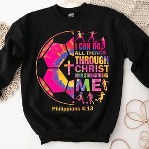 K&ouml;nnte beinhalten: Schwarzer Pullover mit einem Batik-Fu&szlig;ball-Motiv und dem Text "Ich kann alles durch Christus, der mich st&auml;rkt" und "Philipper 4:13".