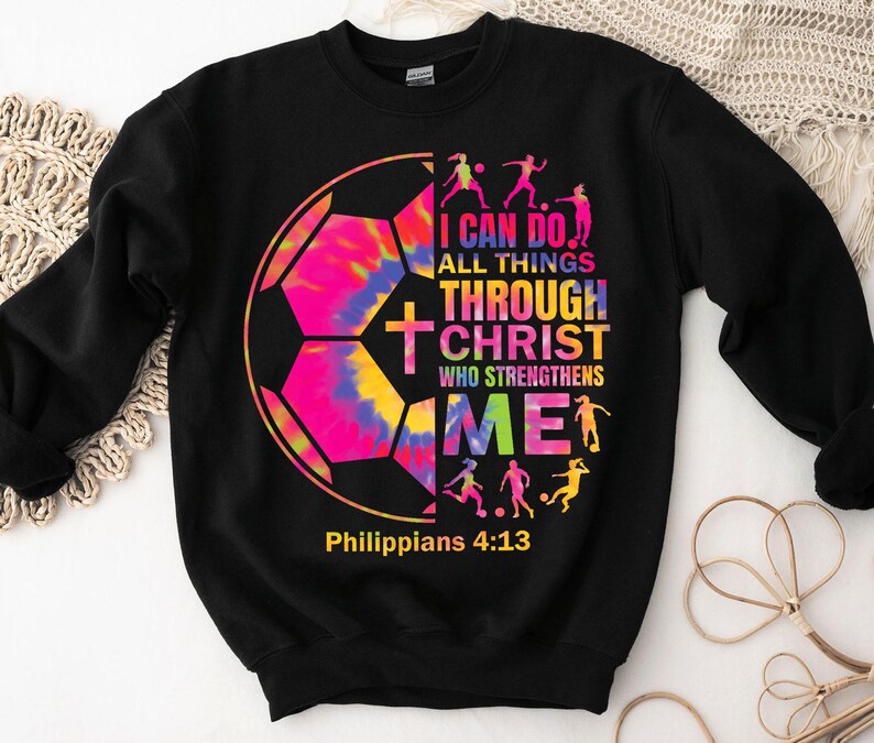 K&ouml;nnte beinhalten: Schwarzer Pullover mit einem Batik-Fu&szlig;ball-Motiv und dem Text "Ich kann alles durch Christus, der mich st&auml;rkt" und "Philipper 4:13".