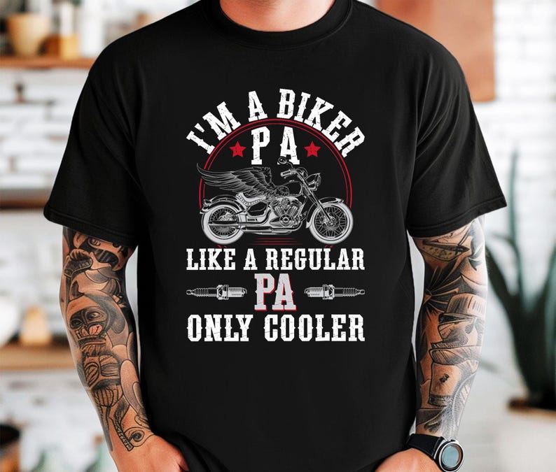 Puede incluir: Camiseta negra con un dise&ntilde;o gr&aacute;fico blanco que dice "I'm a biker PA like a regular PA only cooler". El gr&aacute;fico tambi&eacute;n incluye una motocicleta y buj&iacute;as.