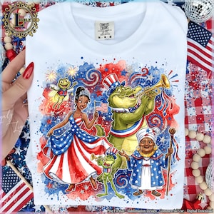 Könnte beinhalten: Weißes T-Shirt mit einem patriotischen Design mit Zeichentrickfiguren in Rot, Weiß und Blau. Das Design umfasst eine Prinzessin, ein Alligator, der Trompete spielt, und einen Frosch. Das Shirt hat den Text "COMFORT COLORS".