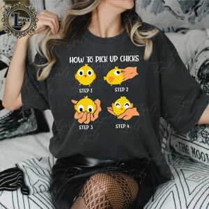 May include: Dark gray t-shirt with the text "HOW TO PICK UP CHICKS" and a four-step graphic of a yellow chick being picked up. The graphic shows the chick in different poses, with the steps labeled 1 through 4.