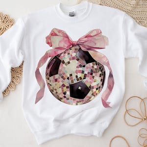 K&ouml;nnte beinhalten: Wei&szlig;er Pullover mit einer rosa Schleife und einem Discokugel-Fu&szlig;ball-Motiv.