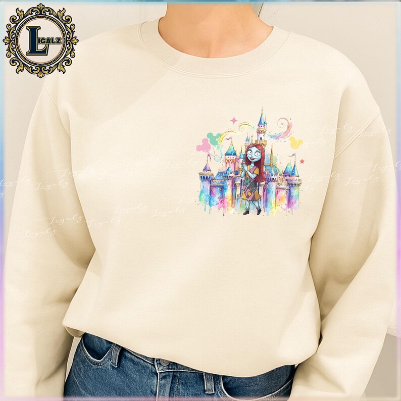 Puede incluir: Sudadera de color crema con una colorida ilustraci&oacute;n de acuarela de un castillo y un personaje. El gr&aacute;fico incluye un castillo con m&uacute;ltiples torres y un personaje con cabello rojo y un vestido de retazos. La sudadera tiene cuello redondo y mangas largas.