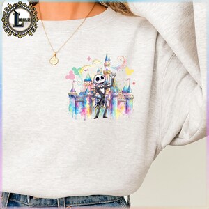 Puede incluir: Una sudadera gris claro con una ilustraci&oacute;n de acuarela de Jack Skellington frente a un castillo colorido. El dise&ntilde;o incluye arco&iacute;ris, estrellas y colores pastel, creando un tema caprichoso.