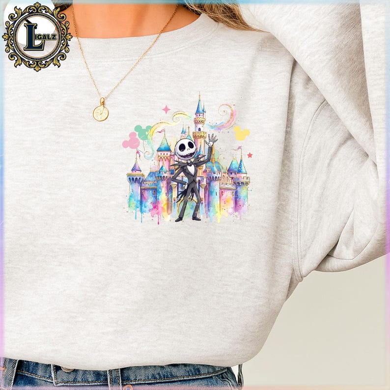 Puede incluir: Una sudadera gris claro con una ilustraci&oacute;n de acuarela de Jack Skellington frente a un castillo colorido. El dise&ntilde;o incluye arco&iacute;ris, estrellas y colores pastel, creando un tema caprichoso.