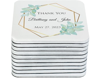 May include: A stack of 12 white square coasters with a gold geometric frame and green watercolor leaves. The text on the coaster reads "Thank You Brittany and John May 27, 2023".