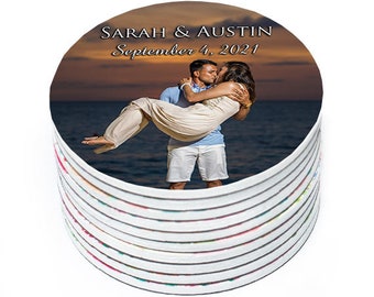 May include: A stack of round white coasters with a printed image of a couple kissing on a beach at sunset. The text "Sarah & Austin September 4, 2021" is printed on the coaster.