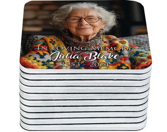May include: A stack of white coasters with a photograph of an elderly woman wearing glasses and a colorful sweater. The text "IN LOVING MEMORY Julia Blake 1953-2024" is printed on the coaster.