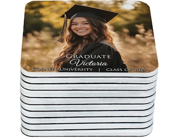 May include: Stack of square coasters featuring a smiling graduate in a cap and gown. The coasters have a photo of a woman with the text "GRADUATE Victoria, Cornell University, Class of 2029". The coasters have a white and black striped edge.