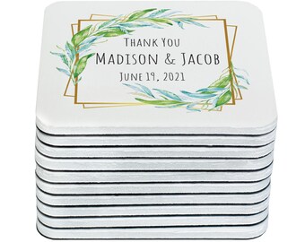 May include: A stack of 12 white square coasters with a gold frame and green and blue watercolor leaves. The text on the coasters reads "Thank You Madison & Jacob June 19, 2021".