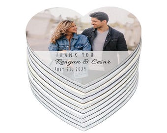 May include: Heart-shaped coasters stacked high, featuring a photo of a couple. The top coaster has the text "THANK YOU Reagan & Cesar JULY 21, 2029". The coasters have a white and gray striped pattern.