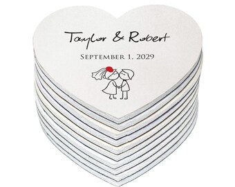 May include: A stack of white heart-shaped wedding favors with the text "Taylor & Robert" and "SEPTEMBER 1, 2029" printed on them. A simple black and white illustration of a bride and groom kissing is also printed on the favors.