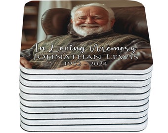 May include: A stack of square coasters featuring a smiling older man in a chair. The coasters have a white border and a printed image with the text "In Loving Memory" and the name "Johnathan Lewis" with the years "1952 - 2024".
