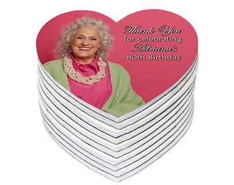 May include: A stack of pink heart-shaped thank you cards with a photo of an older woman with curly hair. The text on the card reads "Thank You for celebrating Adriana's 80th Birthday."