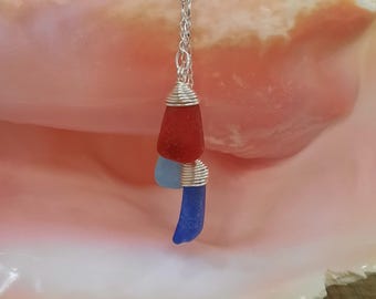 May include: A silver chain necklace with a pendant made of three pieces of sea glass. The top piece is red, the middle piece is light blue, and the bottom piece is dark blue. The sea glass pieces are wrapped in silver wire.
