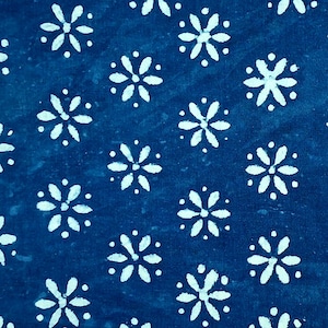 May include: A rectangular piece of fabric featuring a deep blue background with a repeating pattern of white, six-petalled floral shapes. The textile has a consistent, evenly spaced print across the entire visible surface, showcasing a simple, repetitive design.