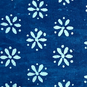 May include: A folded piece of fabric featuring a deep blue background with a repeating white floral pattern. The design consists of small, six-petaled flowers arranged in a grid-like formation across the entire visible surface of the textile.