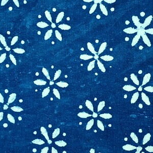 Pode incluir: Um tecido azul profundo com um padr&atilde;o repetitivo de motivos florais brancos de seis p&eacute;talas. Cada flor &eacute; rodeada por pequenos pontos brancos, criando um design consistente e sim&eacute;trico em toda a superf&iacute;cie do material t&ecirc;xtil.