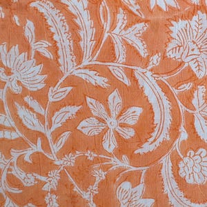 Könnte beinhalten: Orangener Stoff mit einem weißen Blumenmuster. Das Muster zeigt komplizierte Blätter und Blüten.