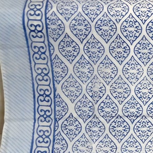 May include: A white cotton tablecloth with a blue and white geometric pattern. The tablecloth has a border of blue and white stripes.