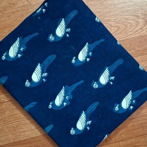 May include: A folded piece of dark blue fabric featuring a repeating pattern of stylised parrots. The birds are rendered in a lighter shade of blue with white wing details, arranged in a diagonal orientation across the entire surface of the textile.