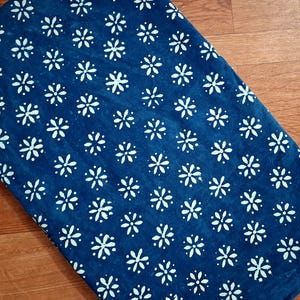 Pode incluir: Uma pe&ccedil;a de tecido retangular com um fundo azul profundo e um padr&atilde;o repetitivo de pequenas flores brancas de seis p&eacute;talas dispostas em grade. O tecido tem uma apar&ecirc;ncia plana e consistente com um contraste claro entre o azul e o branco.