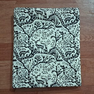 May include: A rectangular piece of fabric featuring a repeating pattern of black deer silhouettes interspersed among black stylized tree branches and foliage against a solid off-white background, folded into a neat, flat, rectangular shape.