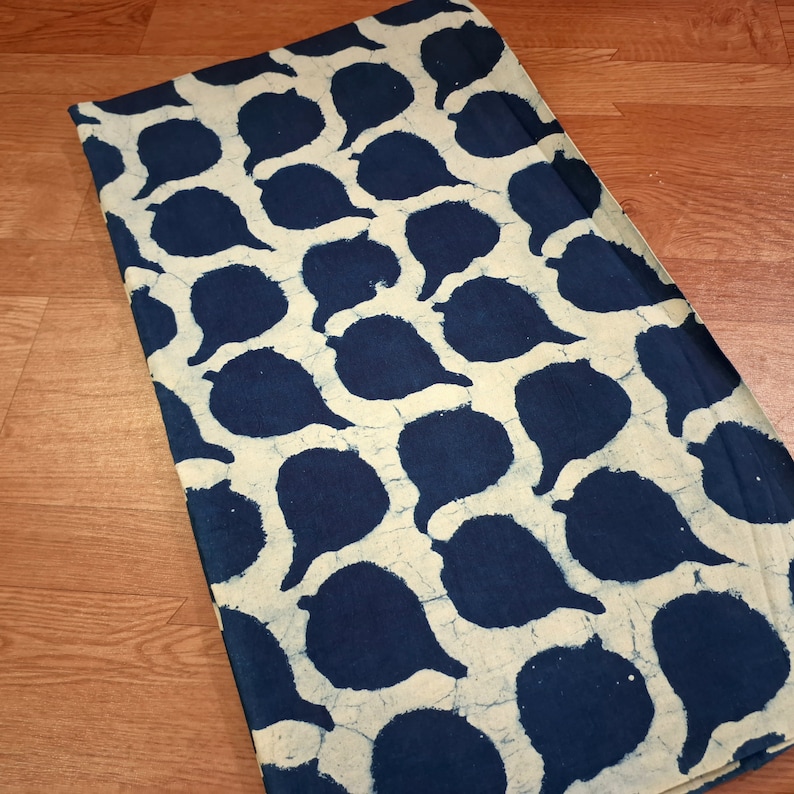 Puede incluir: Una tela blanca con un patr&oacute;n batik azul de formas de l&aacute;grima. La tela tiene una superficie ligeramente texturizada.