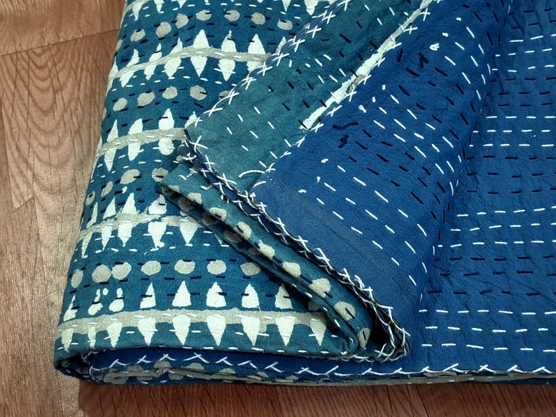 Puede incluir: Una colcha kantha azul y blanca con un patr&oacute;n geom&eacute;trico. La colcha est&aacute; doblada por la mitad y la tela es texturizada.
