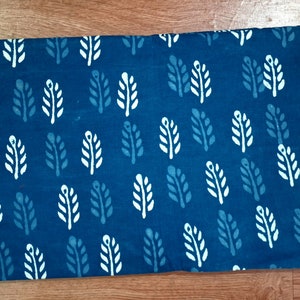 May include: A blue fabric with a white leaf pattern. The fabric is folded in half and has a smooth texture.