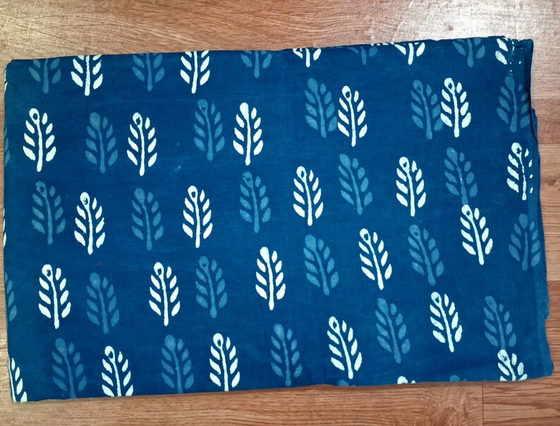 May include: A blue fabric with a white leaf pattern. The fabric is folded in half and has a smooth texture.
