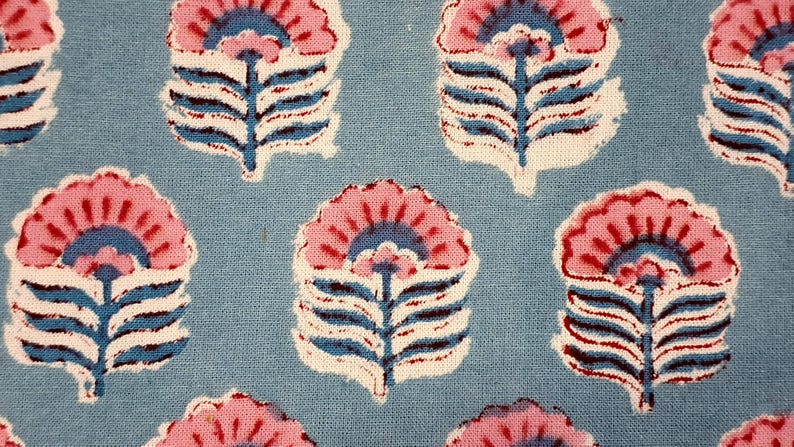 May include: Close-up of a blue fabric with a repeating floral pattern. The flowers are pink with blue and white accents, and the stems are blue. The fabric has a textured appearance.