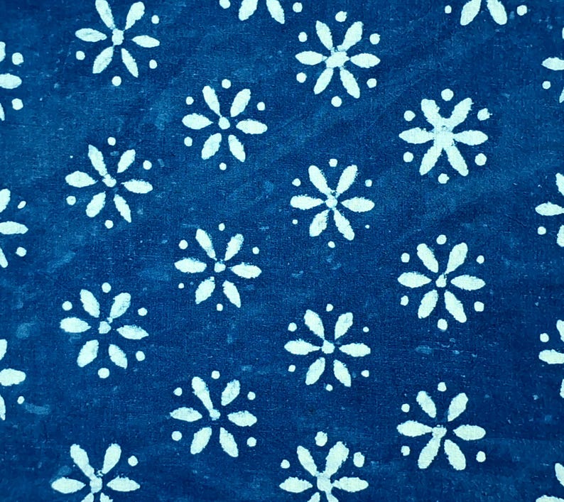 Pode incluir: Um tecido azul profundo com um padr&atilde;o repetitivo de motivos florais brancos de seis p&eacute;talas. Cada flor &eacute; rodeada por pequenos pontos brancos, criando um design consistente e sim&eacute;trico em toda a superf&iacute;cie do material t&ecirc;xtil.