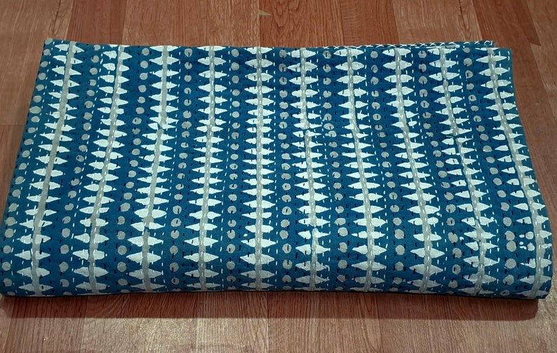 Puede incluir: Una tela de algod&oacute;n azul y blanco con un dise&ntilde;o geom&eacute;trico. La tela est&aacute; doblada por la mitad y est&aacute; sobre una superficie de madera.