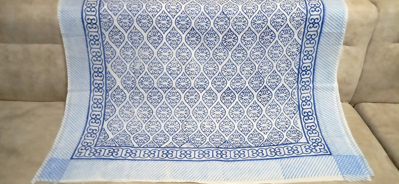 May include: A white cotton tablecloth with a blue and white geometric pattern. The tablecloth has a border of blue and white stripes.