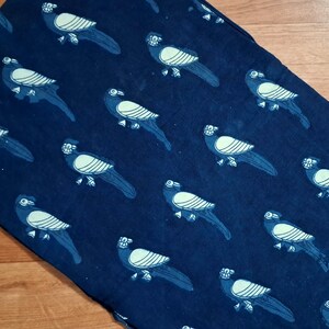 May include: A rectangular fabric textile featuring a repeating pattern of stylised birds in light blue against a deep navy blue background. The birds are depicted in profile with striped wing details and long tail feathers, arranged in a grid-like layout.