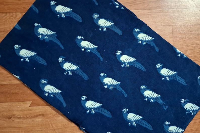 May include: A rectangular fabric textile featuring a repeating pattern of stylised birds in light blue against a deep navy blue background. The birds are depicted in profile with striped wing details and long tail feathers, arranged in a grid-like layout.