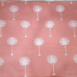 May include: A coral-colored fabric with a repeating pattern of white palm tree designs. The palm trees are embroidered with detailed fronds and slender trunks, creating a tropical aesthetic. The fabric is likely used for home decor or apparel.