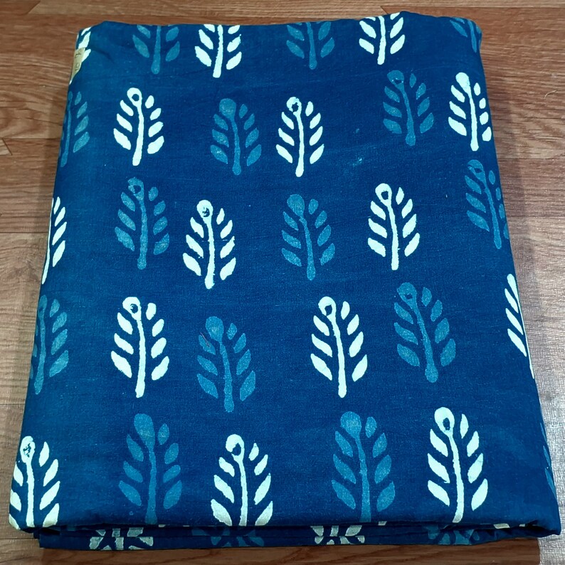 May include: A blue fabric with a white and light blue leaf pattern. The fabric is folded in half.