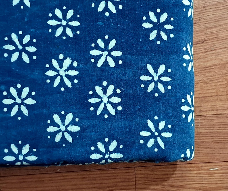 May include: A folded piece of fabric featuring a deep blue background with a repeating white floral pattern. The design consists of small, six-petaled flowers arranged in a grid-like formation across the entire visible surface of the textile.