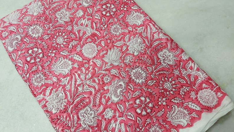 K&ouml;nnte beinhalten: Rosa Baumwollstoff mit wei&szlig;em Blumendruck. Der Stoff hat eine weiche, flie&szlig;ende Textur und ist perfekt f&uuml;r Bastelprojekte.