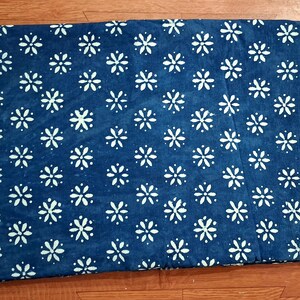 Pode incluir: Uma pe&ccedil;a de tecido retangular com um fundo azul profundo e um padr&atilde;o repetitivo de flores brancas de seis p&eacute;talas dispostas em grade. O tecido tem uma apar&ecirc;ncia plana e consistente com bordas n&iacute;tidas e um design floral uniforme.
