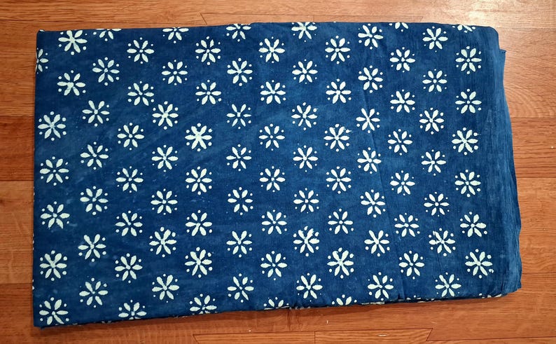 Pode incluir: Uma pe&ccedil;a de tecido retangular com um fundo azul profundo e um padr&atilde;o repetitivo de flores brancas de seis p&eacute;talas dispostas em grade. O tecido tem uma apar&ecirc;ncia plana e consistente com bordas n&iacute;tidas e um design floral uniforme.