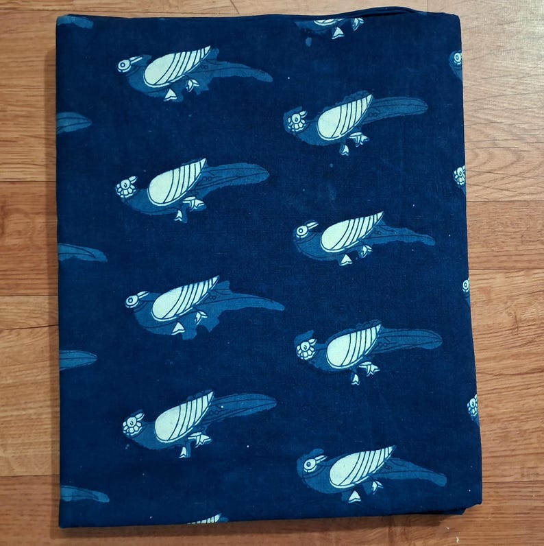 May include: A rectangular piece of dark navy blue fabric featuring a repeating pattern of light blue birds. Each bird is depicted in profile with stylised wings and a long tail, arranged in a consistent grid-like layout across the textile surface.