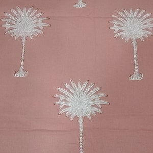 May include: A dusty rose fabric featuring a repeating pattern of white palm trees. The palm trees have detailed fronds and textured trunks, with small red accents. The design is evenly spaced across the textile.