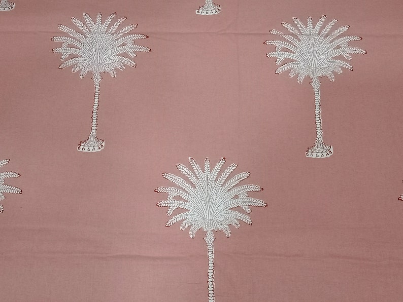 May include: A dusty rose fabric featuring a repeating pattern of white palm trees. The palm trees have detailed fronds and textured trunks, with small red accents. The design is evenly spaced across the textile.