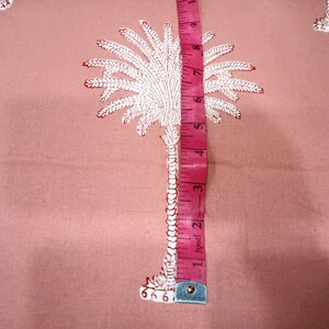 May include: Pink fabric with a repeating white and red palm tree pattern. A pink measuring tape shows a measurement of approximately 5 inches. The fabric is likely used for sewing or crafting projects.