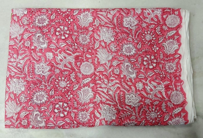 K&ouml;nnte beinhalten: Rosa Stoff mit wei&szlig;em Blumendruck. Der Stoff hat eine weiche, flie&szlig;ende Textur und ist perfekt f&uuml;r Bastel- oder N&auml;hprojekte.