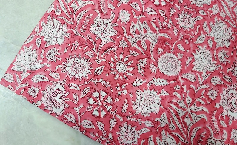 K&ouml;nnte beinhalten: Rosafarbener Stoff mit einem wei&szlig;en Blumenmuster. Der Stoff hat einen dezenten Batik-Effekt.