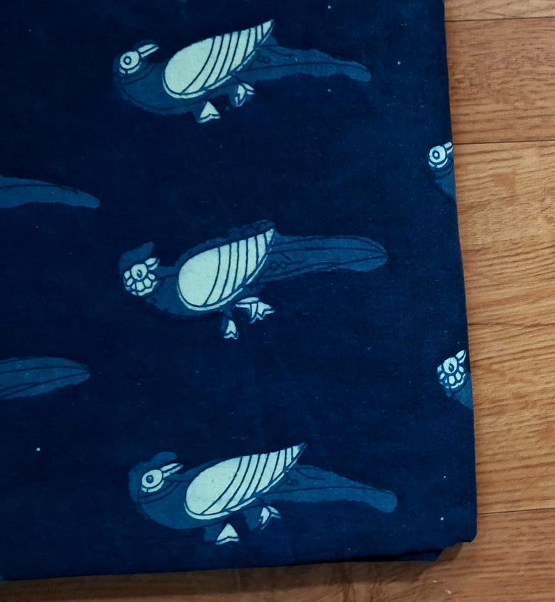 May include: A dark navy blue fabric featuring a repeating pattern of stylised birds in a lighter blue shade. Each bird is depicted in profile with a prominent wing, a long tail, and a small crest on its head, arranged in a consistent horizontal layout.